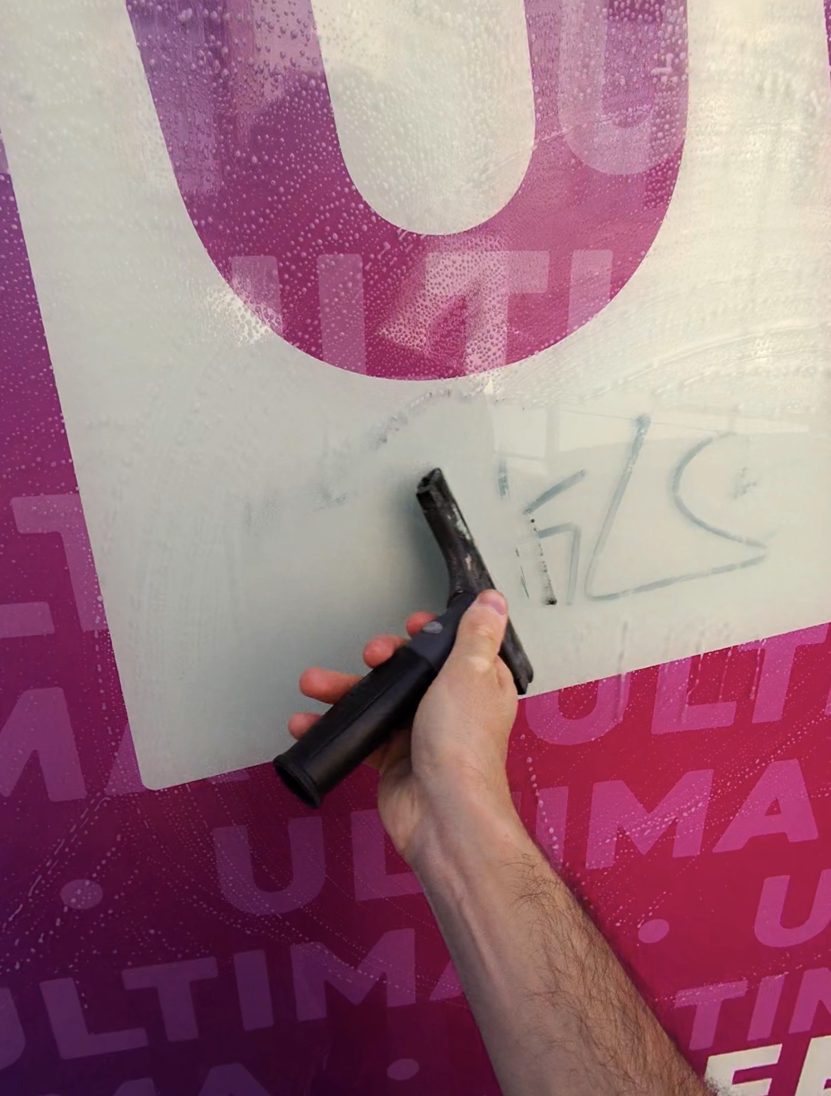 Passage d'un grattoir à lame inox sur une vitre encrassée